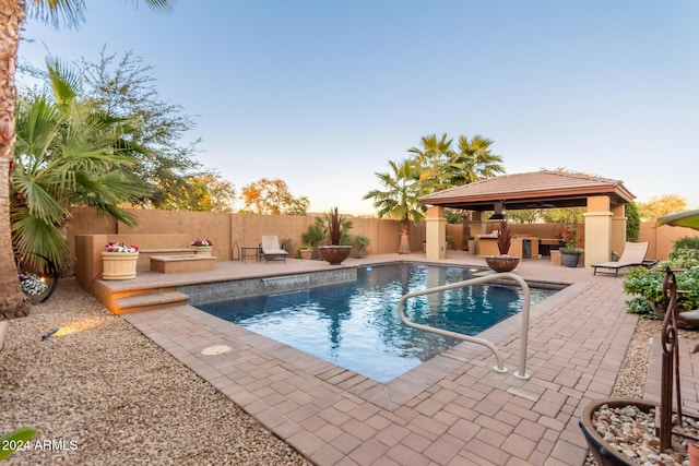 pool at dusk with a patio area and a gazebo