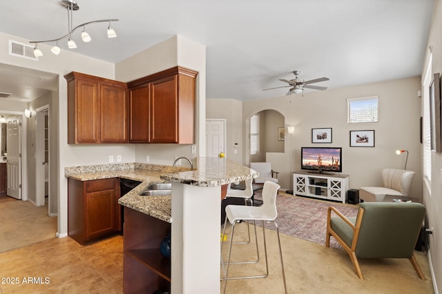 kitchen featuring visible vents, a breakfast bar, ceiling fan, arched walkways, and a sink