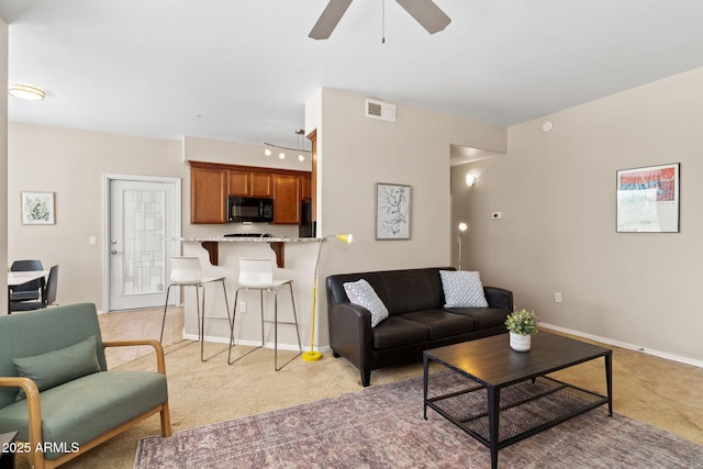 living room featuring a ceiling fan, light carpet, baseboards, and visible vents