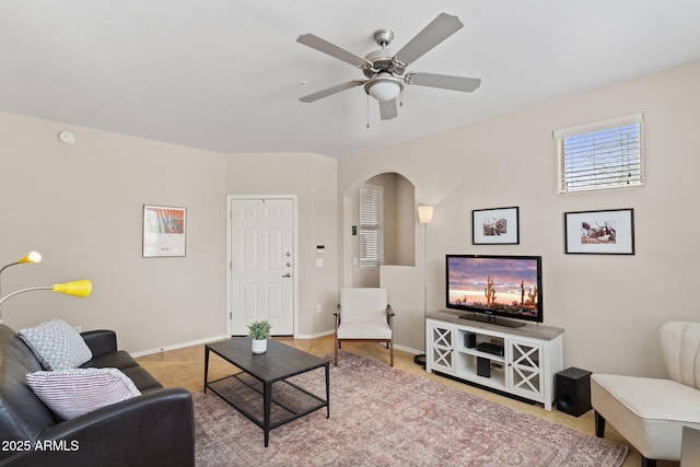 living area featuring arched walkways, baseboards, and a ceiling fan