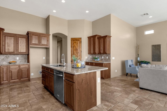 kitchen featuring backsplash, stainless steel dishwasher, a center island with sink, and sink