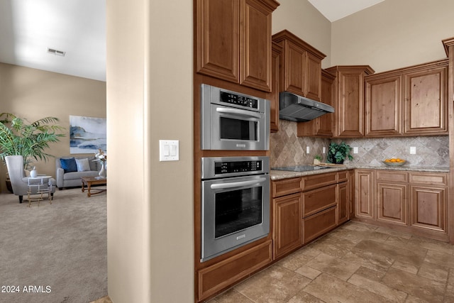 kitchen with black electric stovetop, light colored carpet, stainless steel double oven, light stone countertops, and decorative backsplash