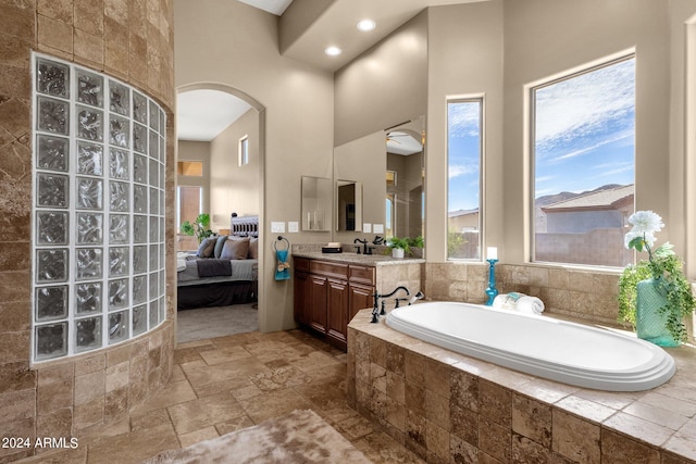 bathroom with a relaxing tiled tub, a towering ceiling, and vanity