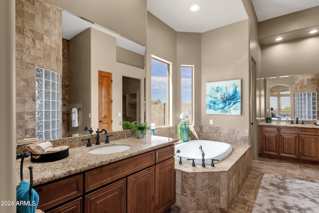 bathroom featuring a relaxing tiled tub, vanity, and a wealth of natural light