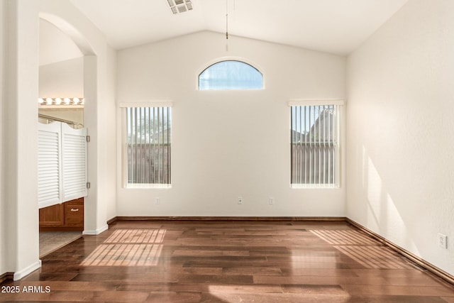 spare room featuring wood finished floors, visible vents, baseboards, lofted ceiling, and arched walkways