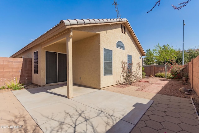 back of property with a tiled roof, stucco siding, a fenced backyard, and a patio area