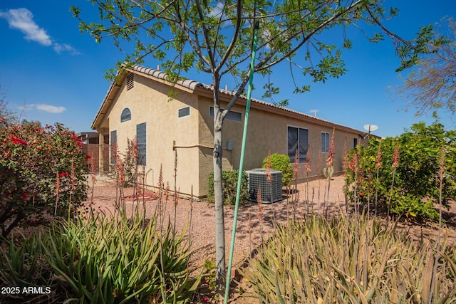 view of property exterior with stucco siding, fence, cooling unit, and a tile roof