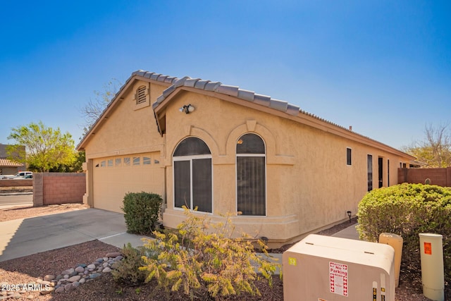 view of home's exterior with stucco siding, fence, concrete driveway, a garage, and a tiled roof