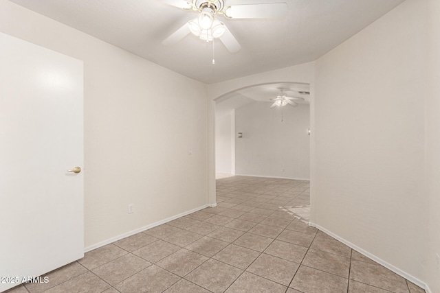 empty room with light tile patterned floors, baseboards, arched walkways, and ceiling fan