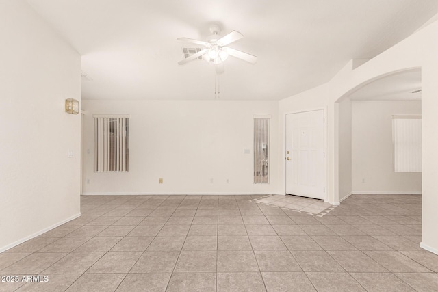 spare room featuring light tile patterned floors, a ceiling fan, visible vents, baseboards, and arched walkways