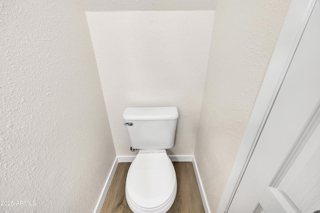 bathroom with baseboards, toilet, wood finished floors, and a textured wall