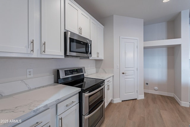 kitchen with light stone countertops, white cabinetry, appliances with stainless steel finishes, and light hardwood / wood-style flooring