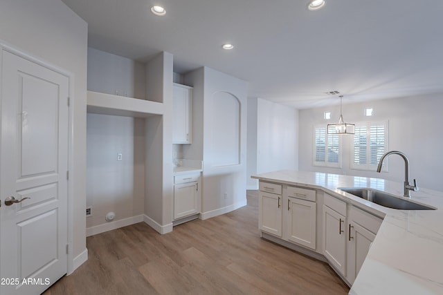 kitchen with pendant lighting, white cabinetry, sink, light stone countertops, and light wood-type flooring