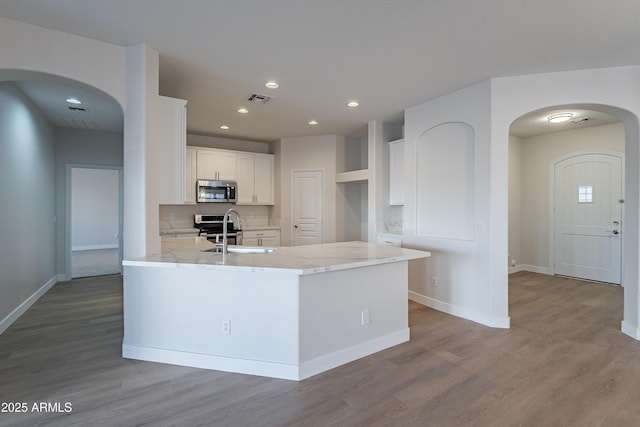 kitchen featuring sink, appliances with stainless steel finishes, light stone countertops, white cabinets, and light wood-type flooring