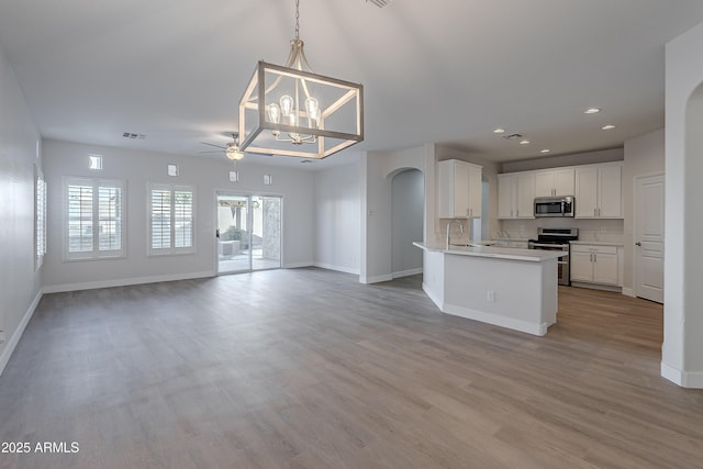 kitchen with an island with sink, white cabinets, hanging light fixtures, light hardwood / wood-style floors, and stainless steel appliances