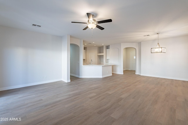 unfurnished living room with hardwood / wood-style floors, sink, and ceiling fan with notable chandelier