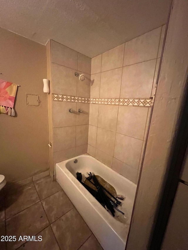 bathroom featuring toilet, tiled shower / bath combo, tile patterned flooring, and a textured ceiling