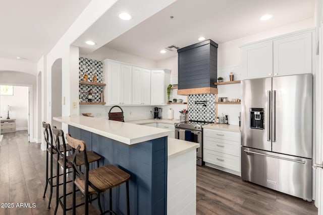 kitchen featuring open shelves, appliances with stainless steel finishes, arched walkways, a kitchen breakfast bar, and visible vents