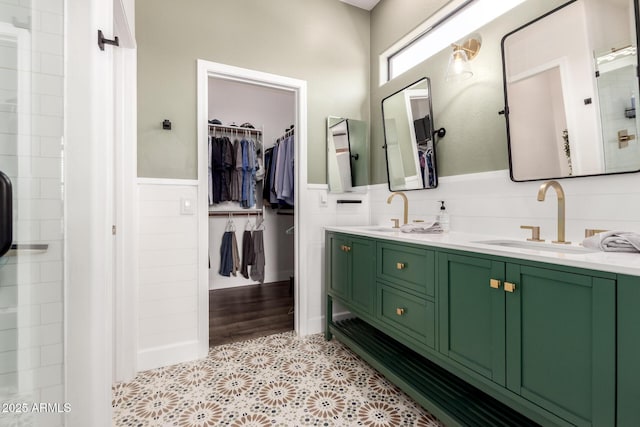 bathroom with a sink, a wainscoted wall, double vanity, and a spacious closet