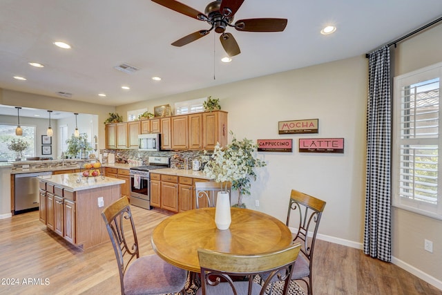 kitchen featuring appliances with stainless steel finishes, hanging light fixtures, light stone counters, a wealth of natural light, and a kitchen island