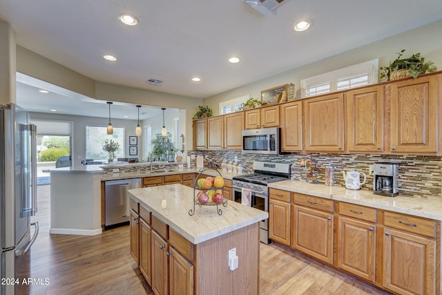 kitchen with hanging light fixtures, appliances with stainless steel finishes, a center island, and kitchen peninsula