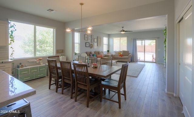 dining area with ceiling fan with notable chandelier, a wealth of natural light, and light hardwood / wood-style floors