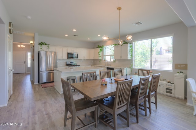 dining area with sink, light wood-type flooring, and an inviting chandelier