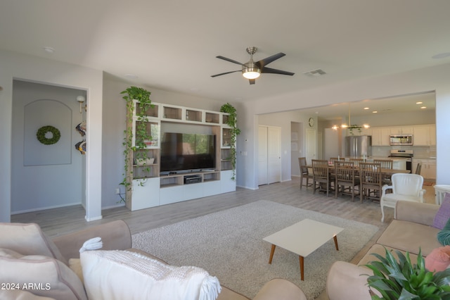 living room with ceiling fan with notable chandelier and light hardwood / wood-style flooring