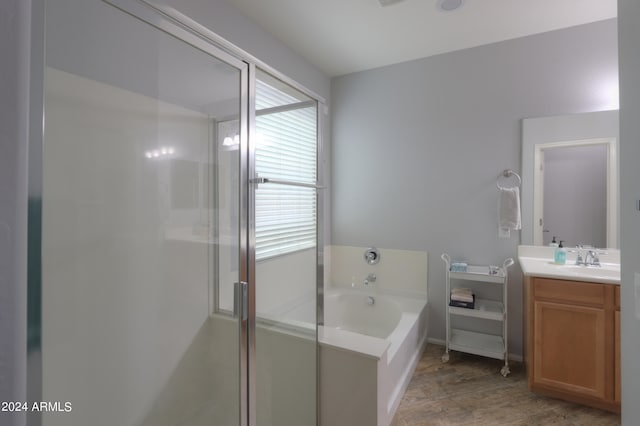 bathroom with hardwood / wood-style floors, vanity with extensive cabinet space, and shower with separate bathtub