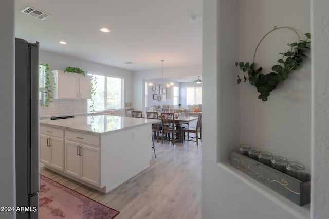 kitchen with tasteful backsplash, stainless steel refrigerator, white cabinets, pendant lighting, and light wood-type flooring