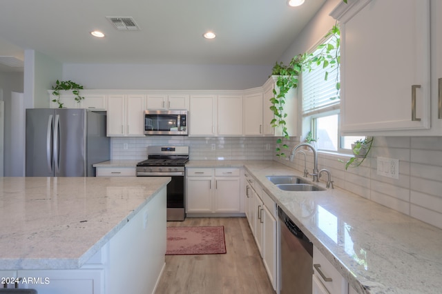 kitchen with appliances with stainless steel finishes, backsplash, light hardwood / wood-style floors, white cabinetry, and sink