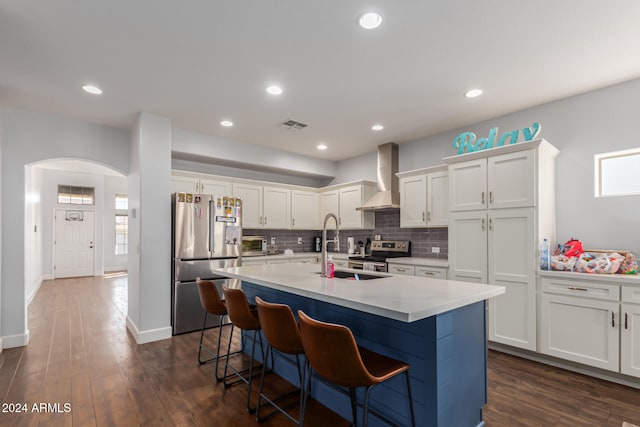 kitchen with a kitchen island with sink, white cabinets, wall chimney range hood, dark hardwood / wood-style floors, and stainless steel appliances