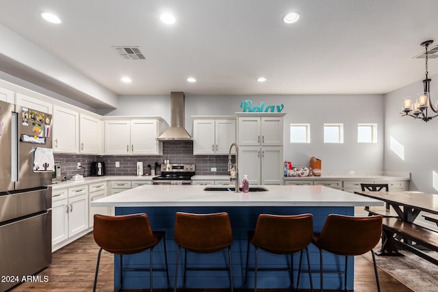 kitchen featuring hanging light fixtures, wall chimney range hood, dark hardwood / wood-style flooring, a kitchen island with sink, and appliances with stainless steel finishes