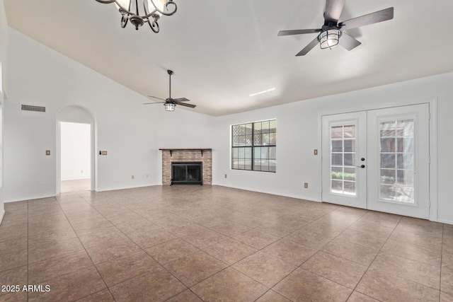 unfurnished living room with ceiling fan with notable chandelier, high vaulted ceiling, light tile patterned floors, a brick fireplace, and french doors