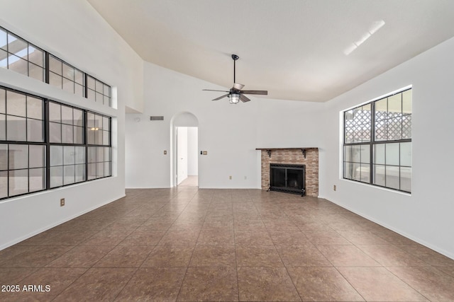 unfurnished living room with tile patterned flooring, a brick fireplace, a towering ceiling, and ceiling fan