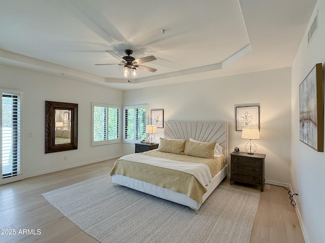 bedroom with visible vents, baseboards, light wood-style floors, and a tray ceiling