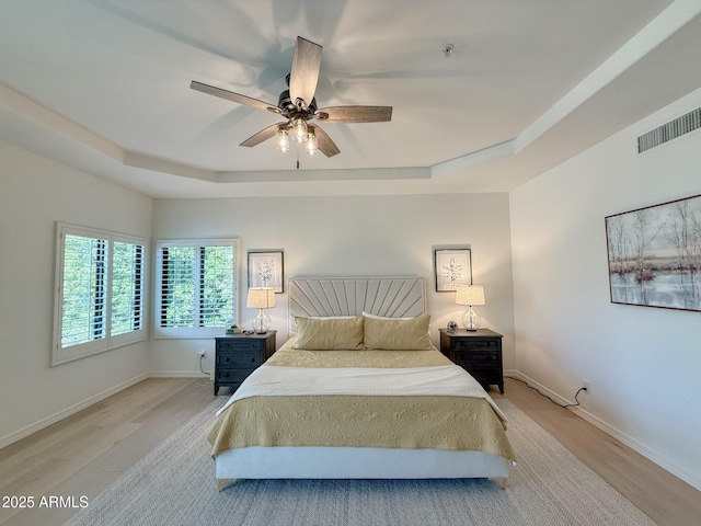 bedroom featuring a raised ceiling, light wood-style floors, baseboards, and visible vents