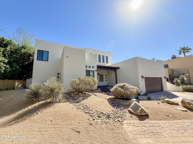 southwest-style home with stucco siding, an attached garage, driveway, and fence