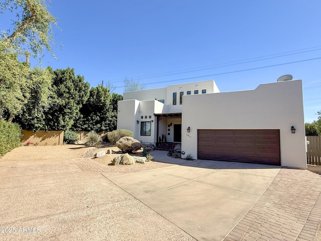 adobe home with stucco siding, driveway, an attached garage, and fence