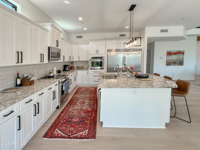 kitchen with visible vents, backsplash, appliances with stainless steel finishes, white cabinets, and a sink