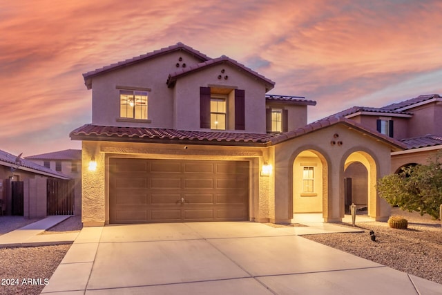 mediterranean / spanish-style home featuring an attached garage, a tile roof, driveway, stucco siding, and fence