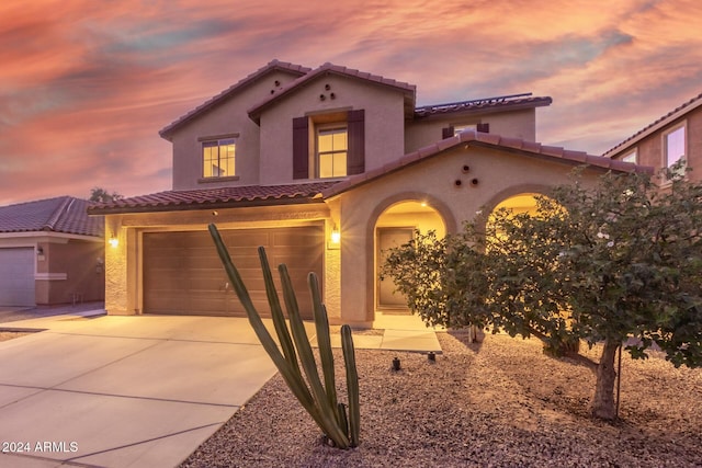 mediterranean / spanish home with a tiled roof, driveway, stucco siding, and an attached garage