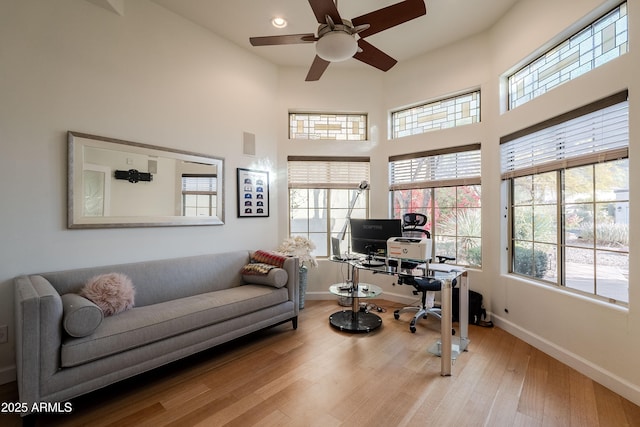 home office with ceiling fan, light hardwood / wood-style flooring, and a towering ceiling