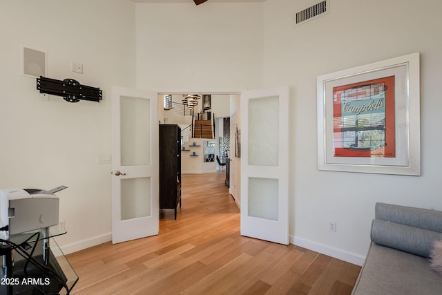 hall with a towering ceiling, light hardwood / wood-style floors, and french doors