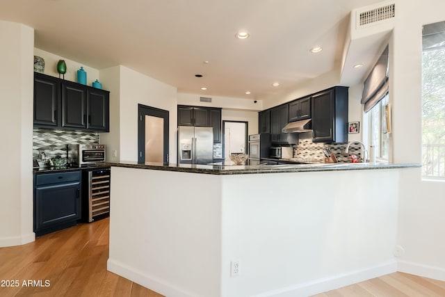 kitchen with beverage cooler, stainless steel appliances, dark stone countertops, kitchen peninsula, and light wood-type flooring