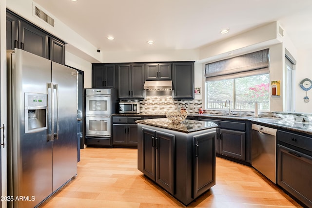 kitchen featuring appliances with stainless steel finishes, a center island, dark stone counters, decorative backsplash, and light hardwood / wood-style flooring