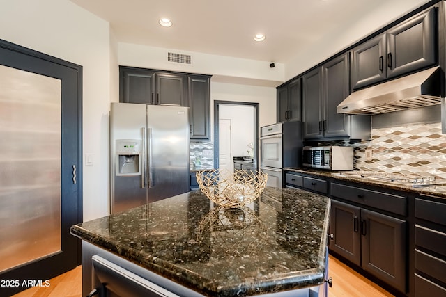 kitchen featuring decorative backsplash, a center island, stainless steel appliances, and dark stone countertops