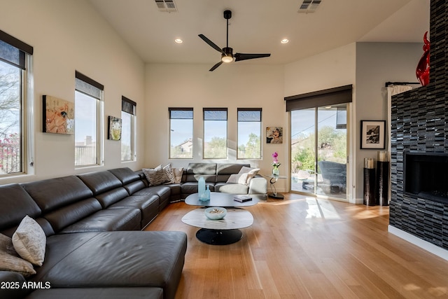 living room featuring ceiling fan, a wealth of natural light, a tiled fireplace, and light wood-type flooring