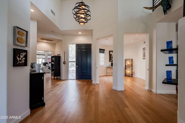 foyer entrance with an inviting chandelier, light hardwood / wood-style floors, and a high ceiling