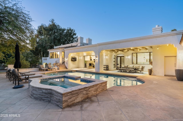 back house at dusk with a swimming pool with hot tub and a patio